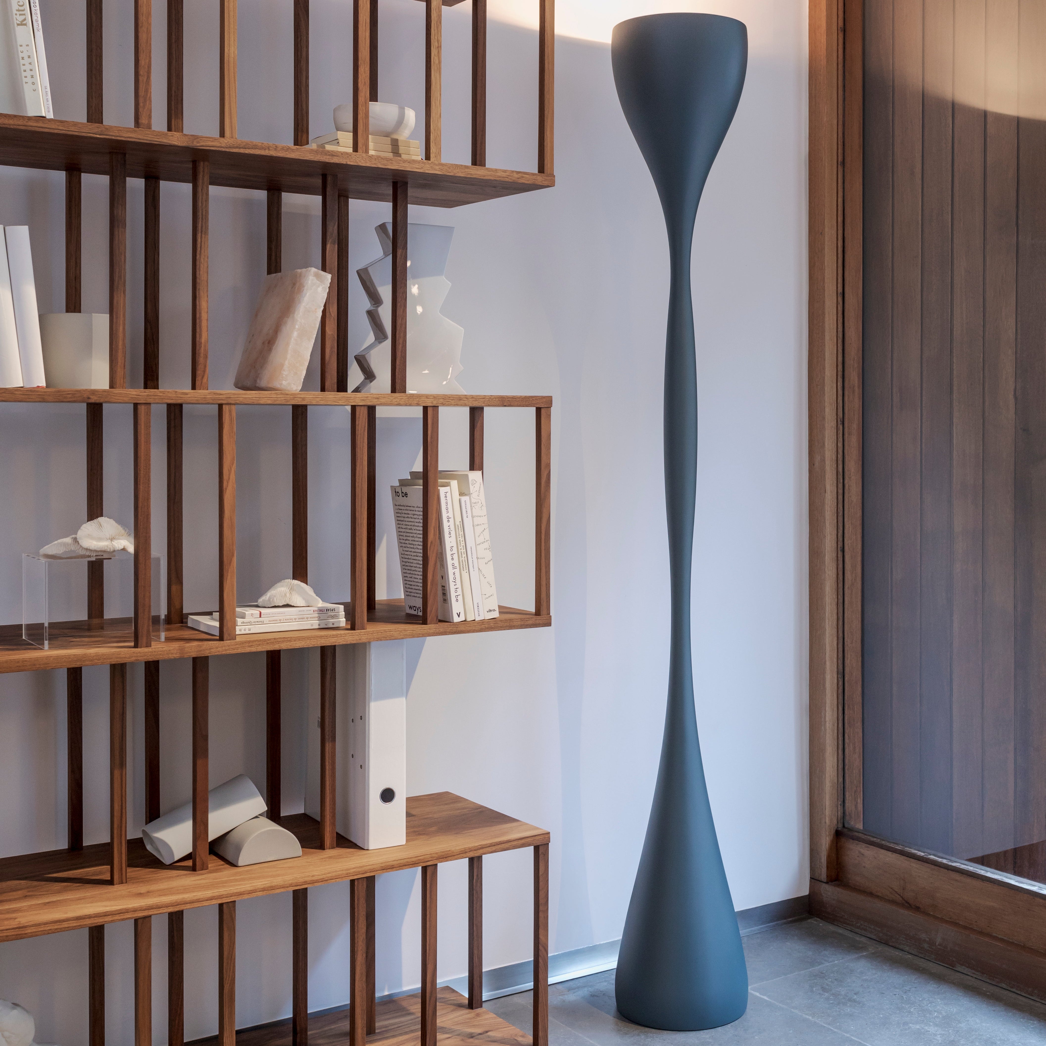 Lampada da terra Jazz di Vibia posizionata vicino alla libreria un soggiorno moderno, che proietta una luce indiretta sul soffitto.